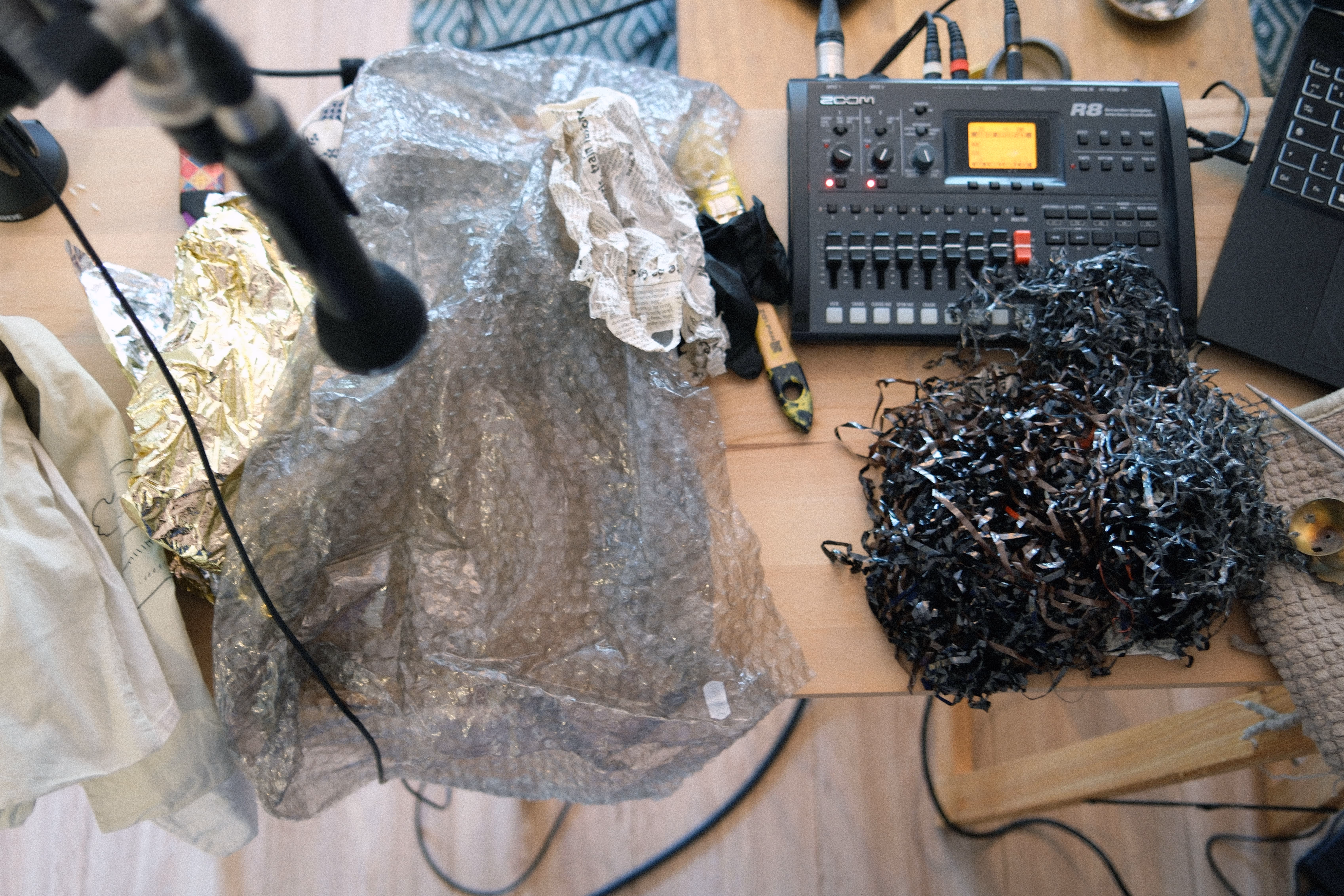 Table de travail avec un enregistreur Zoom R8, des micros et des matériaux pour créer des effets sonores : papier bulle, papier froissé, rubans magnétiques déchiquetés