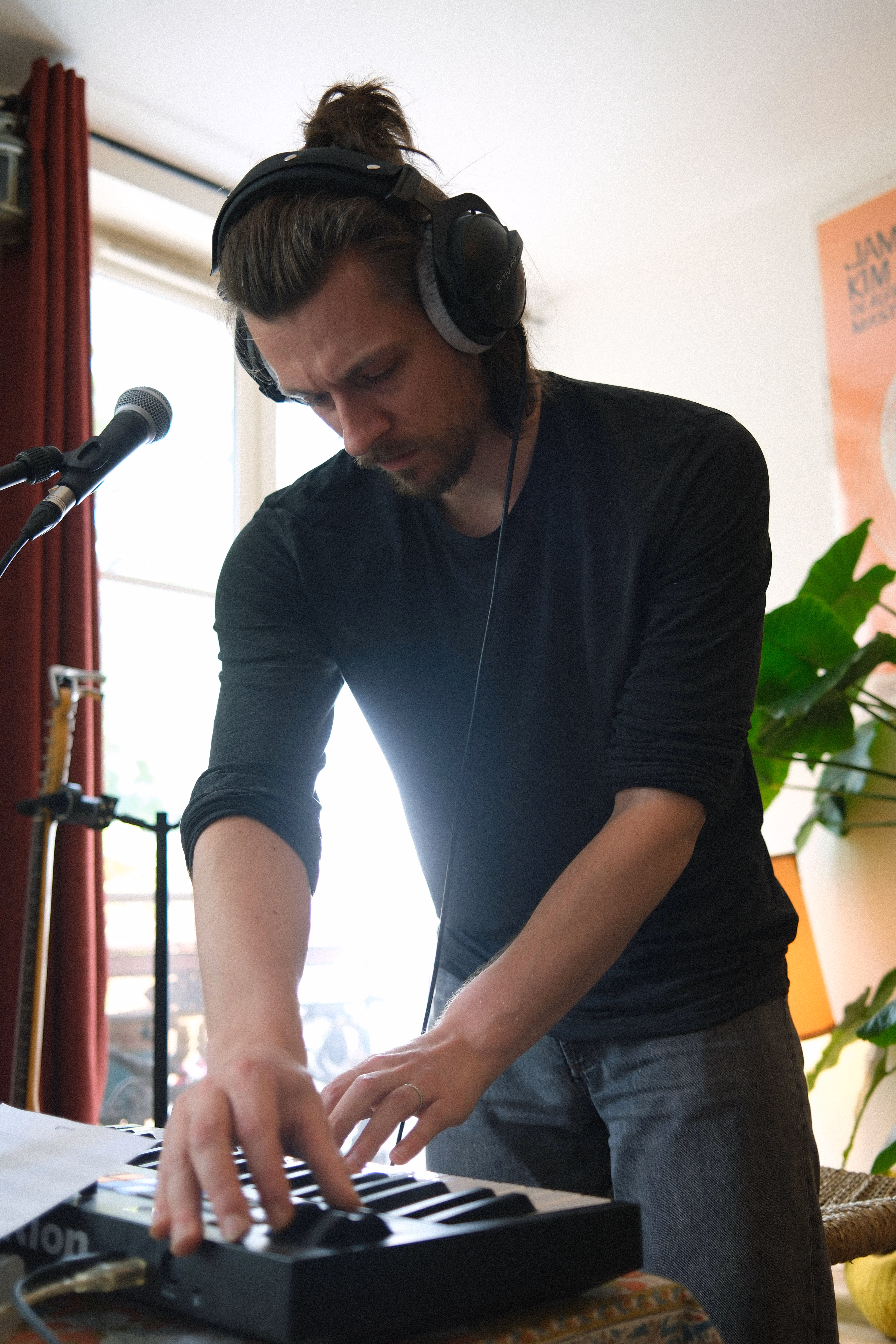 Un homme avec un casque audio joue d'un clavier MIDI, concentré, devant un micro dans un salon